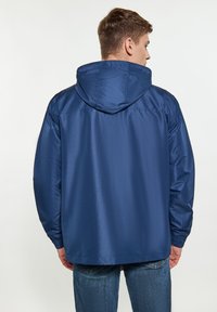 Tamsiai mėlyna su gobtuvu striukė su tekstūruota apdaila, elastinėmis rankogaliais ir laisvuoju siluetu, sukurta komfortui ir apsaugai nuo oro.