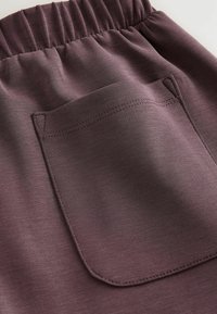 Pantaloni cu talie elastică dintr-un material violet estompat, prevăzuți cu un singur buzunar pe spate, având o cusătură curată și o textură netedă.