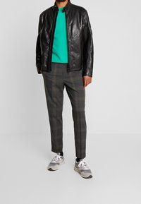 Czarna skórzana kurtka, zielony sweter, szare spodnie w kratę i szare trampki. Kurtka ma zamek z przodu i wysoki kołnierz, a jej design jest smukły.