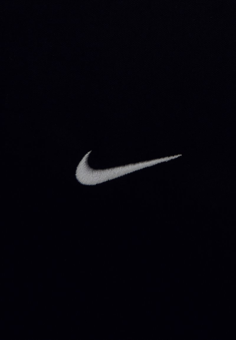 Logotipo de la marca Nike en color blanco bordado sobre un fondo de tela oscura, centrado y claramente visible.