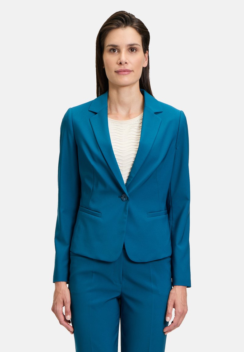 Tömör, kékeszöld blézer, bevarrt hajtókával, egysoros gombolással és két el�ülső zsebből áll, texturált krém színű toppal párosítva.