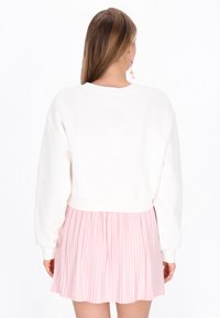 Hvid cropped sweatshirt med lange ærmer, kombineret med en plisseret lyserød nederdel. Outfitet har en glat tekstur og et rent design.