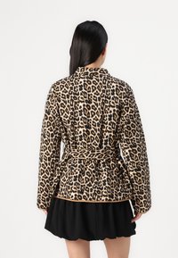 Leopard print jacket in soft fabric, belted at the waist with long sleeves and a collar. Black skirt worn underneath.