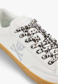 Zapatillas de cuero blancas con cordones de estampado de leopardo y un diseño de calavera y tibias plateadas con brillo. Tiene una suela de goma.