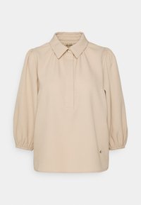 Beige blus med krage, knapplist och puffärmar. Tillverkad av ett slätt tyg med en subtil lyster. Har en dekorativ knappdetalj.