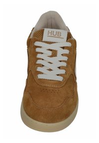 Braune Wildledersneaker mit weißen Schnürsenkeln, perforiertem Zehenbereich und "HUB"-Markenlabel auf der Zunge, Vorderansicht.