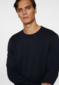 Mörkblå sweatshirt med rundad halsringning och långärmar. Har en subtil logotyp präglad på bröstet och ribbade ärmslut. Mjuk textur.