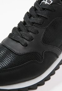 Černá sportovní bota s texturovaným svrškem, síťovanými panely, kulatými tkaničkami a gumovou podešví s bílými a modrými akcenty.