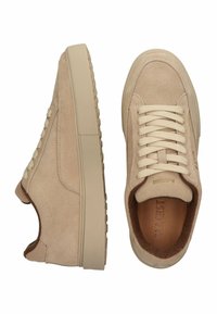 Zapatillas de ante beige con un acabado texturizado, suela plana de goma beige y cordones crema. Presenta un logotipo grabado en la lengüeta.
