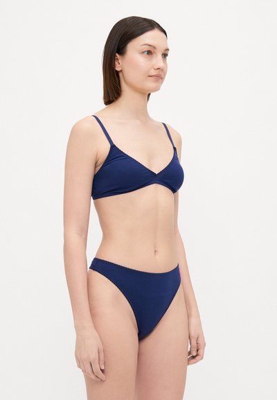 Kleitas zila bikini, kas izgatavots no mīkstas auduma. Iekļauj trīsstūra formas augšdaļu ar regulējamām siksnām un viļņotām malām, kā arī saderīgas augstas jostas bikses.