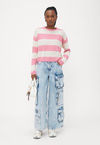 Maglione a righe rosa e bianco, abbinato a jeans cargo larghi azzurri chiari con molte tasche e cerniere. Accessoriato con una borsa bianca.