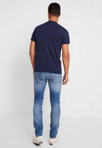 Mörkblå t-shirt med kort ärm i kombination med smalpassande ljusblå jeans. T-shirten har en rundad halsringning, slät yta och avslappnad design.