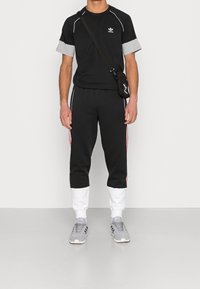 Completo sportivo nero con accenti grigi; maglietta a maniche corte e pantaloni affusolati con polsini bianchi e strisce rosse; abbinato a sneaker grigie.