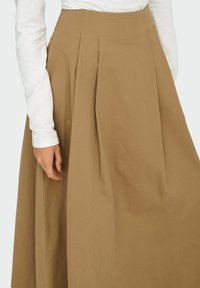 Jupe plissée marron en matière douce et légère. Caractérisée par une taille haute et une texture lisse, avec une forme fluide et ample en ligne A.