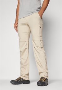 Pantalones cargo beige con bolsillo lateral con cremallera, tejido ligero y diseño de pierna recta, combinados con zapatos de senderismo negros y naranjas.