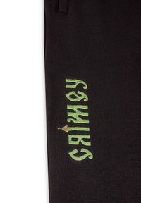 Schwarze Hose mit grüner stickierter Aufschrift "GAMY" und einem kleinen goldenen Turm-Symbol, aus weichem Stoff mit glatter Textur.