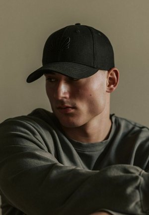 Fekete baseball sapka domború kagyló mintával az elején, szürke kapucnis pulóverrel párosítva, bemutatva a laza szabást és a puha textúrát.