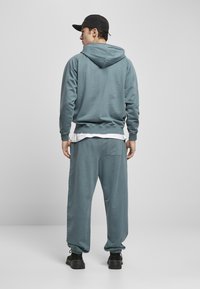 Felpa con cappuccio grigio-blu e pantaloni della tuta coordinati. Tessuto morbido, vestibilità rilassata, polsini a coste e cordino regolabile in vita. Sneakers nere.