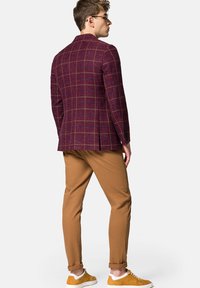 Burgundowy blazer w kratę z wyraźnymi ramionami, dopasowany do brązowych spodni i żółtych sneakersów. Gładki materiał o czystym wykończeniu.