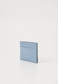Kortholder laget av teksturert lyseblått materiale med fire kortlommer og en kontrasterende svart kant, med et slankt, rektangulært design.