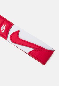 Hvid og rød læderrem med et fremtrædende rødt Nike swoosh-design, detaljeret syning og en struktureret finish.