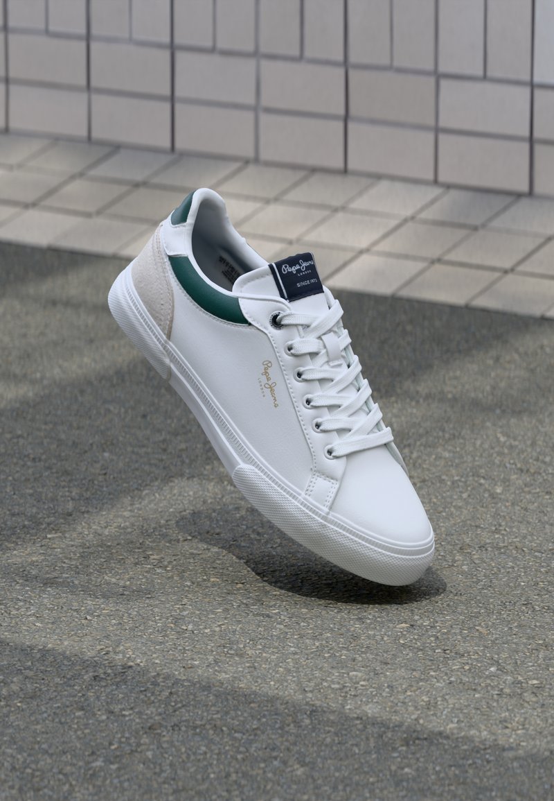 Balti odiniai sportbačiai su žaliais ir smėliniais akcentais, su tekstūruota pado struktūra, apvaliu pirštu ir tradiciniu nėriniuoto dizaino stiliumi.