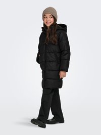 Black, hooded puffer coat with a textured pattern, paired with a beige knitted beanie and black pants. Glossy black shoes complete the outfit.