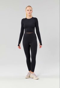 Schwarzes langärmliges Cropped-Top und High-Waist-Leggings aus elastischem Stoff, kombiniert mit hellen Sportschuhen.