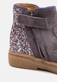 Lilla ruskinds ankelstøvle med en glitrende multicolorer palietbag, lynlås og velcro-lukning samt en tekstureret brun gummisål.