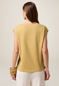 Mustard yellow, short-sleeve top with a relaxed fit and round neckline. Smooth cotton fabric with simple stitching details.