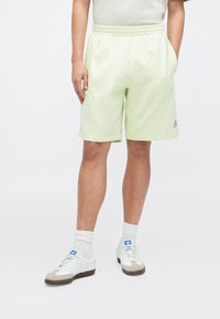 Pantaloni scurți sport de culoare verde deschis, cu talie elastică, buzunare laterale și cusături tonale. Asortați cu adidași albi și șosete deschise.