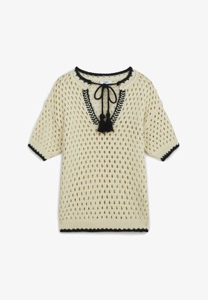 Crème gebreid pullover met open gaasontwerp, zwarte rand rond de halslijn en mouwen, en decoratieve kwastjes bij de halslijn.