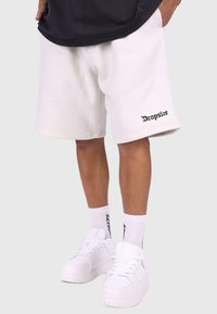 Hvide bomuldsshorts med broderet sort "Dropsize" logo, parret med hvide sneakers og matchende strømper med sort tekst.