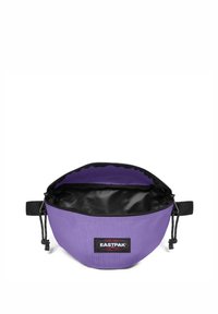 Fialová textilní taška s černým zipem a podšívkou. Obsahuje nášivku s logem Eastpak a na boku má šňůrku pro bezpečné nošení.