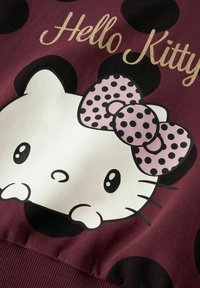 Sudadera burdeos con un gran gráfico de Hello Kitty en blanco, con un lazo de lunares rosas y acentos de lunares negros en el fondo.