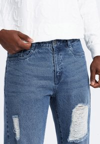 Jeans de mezclilla azul con un corte ajustado, que presentan desgastes y desgarros en las rodillas y un diseño clásico de cinco bolsillos.