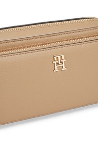 Μπεζ δερμάτινη θήκη με δύο χρυσά φερμουάρ και ένα μικρό χρυσό λογότυπο Tommy Hilfiger στο μπροστινό μέρος.