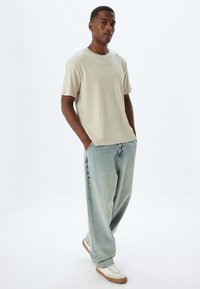 Lichtbeige T-shirt met korte mouwen, ontspannen pasvorm, gecombineerd met lichtblauwe wijde jeans, met een subtiel logo op de voorkant en sneakers.
