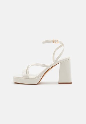 Sandalias blancas de tacón bloque con tiras finas, puntera cuadrada, suela con plataforma y correa ajustable en el tobillo con detalle de hebilla en tono dorado.