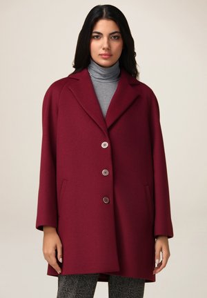 Manteau en mélange de laine bordeaux avec un col à revers, trois boutons et poches latérales. Porté sur un pull col roulé gris, mettant en valeur une coupe décontractée.