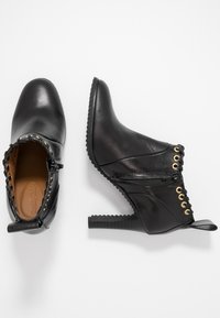 Botas de cuero negras hasta el tobillo, con tacón alto, cordones en la parte delantera con ojetes dorados, superficie texturizada y costuras decorativas en el collar.