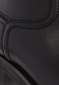 Black leather boot with smooth texture, detailed stitching, and a low heel. Focus on sleek design with a rounded shape.