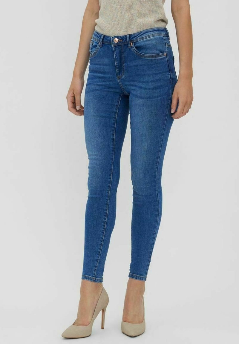 Vaqueros ajustados de mezclilla azul con una cintura alta, cinco bolsillos y un ligero desgastado. Combinados con tacones altos beige para un contraste.