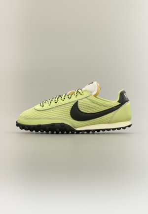Ανοιχτοπράσινο αθλητικό παπούτσι Nike με μαύρη σόλα, μαύρο λογότυπο Swoosh, κορδόνια με σχέδιο και υφασμάτινο πλεκτό επάνω μέρος, σε πλευρική όψη.
