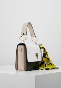 Piccola borsa strutturata con pannelli beige, bianchi e neri, manici dorati a "G", placca logo triangolare e una sciarpa a motivo giallo e nero annodata di lato.