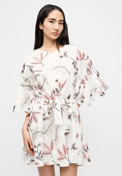 Λευκό φόρεμα με λουλουδάτα σχέδια σε ροζ και μαύρο. Έχει κοντά, φουντωτά μανίκια και ζώνη που δένει στη μέση, κατασκευασμένο από ελαφρύ ύφασμα.