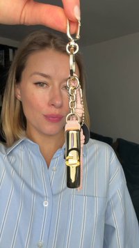 Sleutelhanger met een zwart en goud cilindervormig stuk, roze leren accenten en gouden beslag. Inclusief een gouden haak en schakelkettingen.