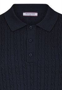 Mørkeblå strikket polo med kabelstrikdesign, der har en klassisk krave og tre sorte knapper ved knaplukningen. Brandskilt synligt.