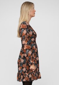 Bloemjurk met een herfstbladprint in oranje, bruin en turquoise op een zwarte achtergrond; met een gerimpelde zoom, lange mouwen en een aansluitend lijfje.