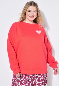 Sweatshirt rouge surdimensionné avec un graphique en forme de cœur blanc "DON'T". Matériau doux, col rond, coutures d'épaules tombantes. Associé à un pantalon à motifs.
